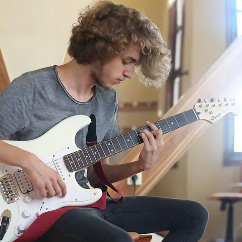 Beyaz elektro gitarla çalışma yapan müzisyen