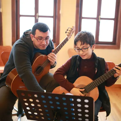 Nota sehpası önünde öğretmen eşliğinde gitar çalışması