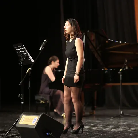 Piyano eşliğinde mikrofon başında şan performansı