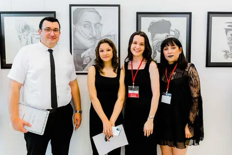 Sergilenen karakalem portrelerin önünde grup fotoğrafı