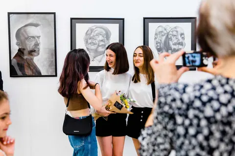 Portre resimlerinin önünde çiçeklerle hatıra fotoğrafı